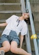 A woman in a white shirt and blue shorts sitting on a set of stairs.