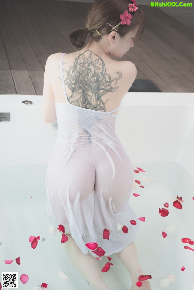 A woman in a white dress sitting in a bathtub with rose petals.