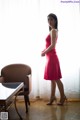 A woman in a red dress standing in front of a window.