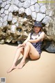 A woman sitting on the sand in front of a stone wall.