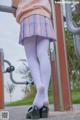 A woman in a pink sweater and purple skirt is standing on a playground.