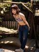 A woman in a bikini top and jeans standing on a wooden deck.